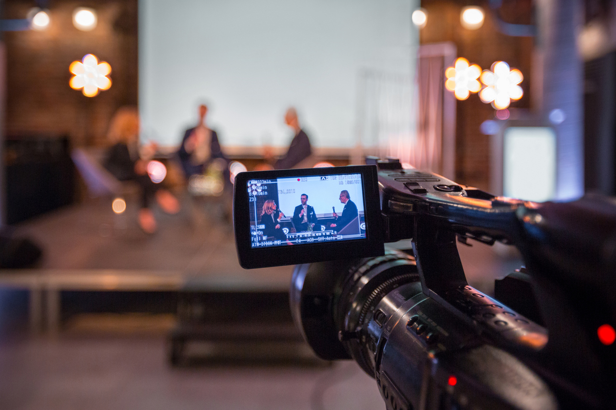 Businesswoman and businessmen during online seminar Businesswoman and businessmen discussing during online seminar, sitting on armchairs on the stage. Focus on video camera.